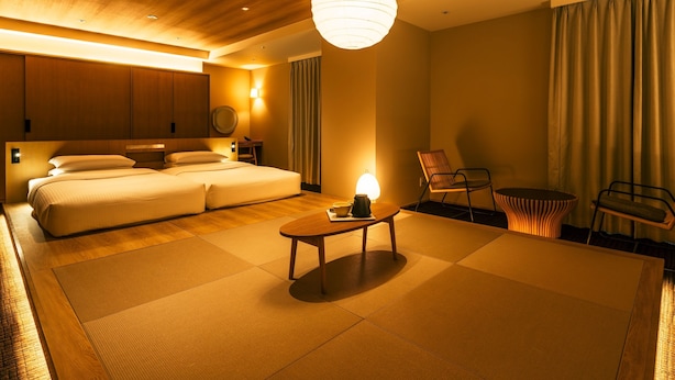 Une chambre d’hôtel moderne dotée d’un grand lit, d’un coin salon avec une table et des chaises, et offrant une vue sur la ville par la fenêtre.