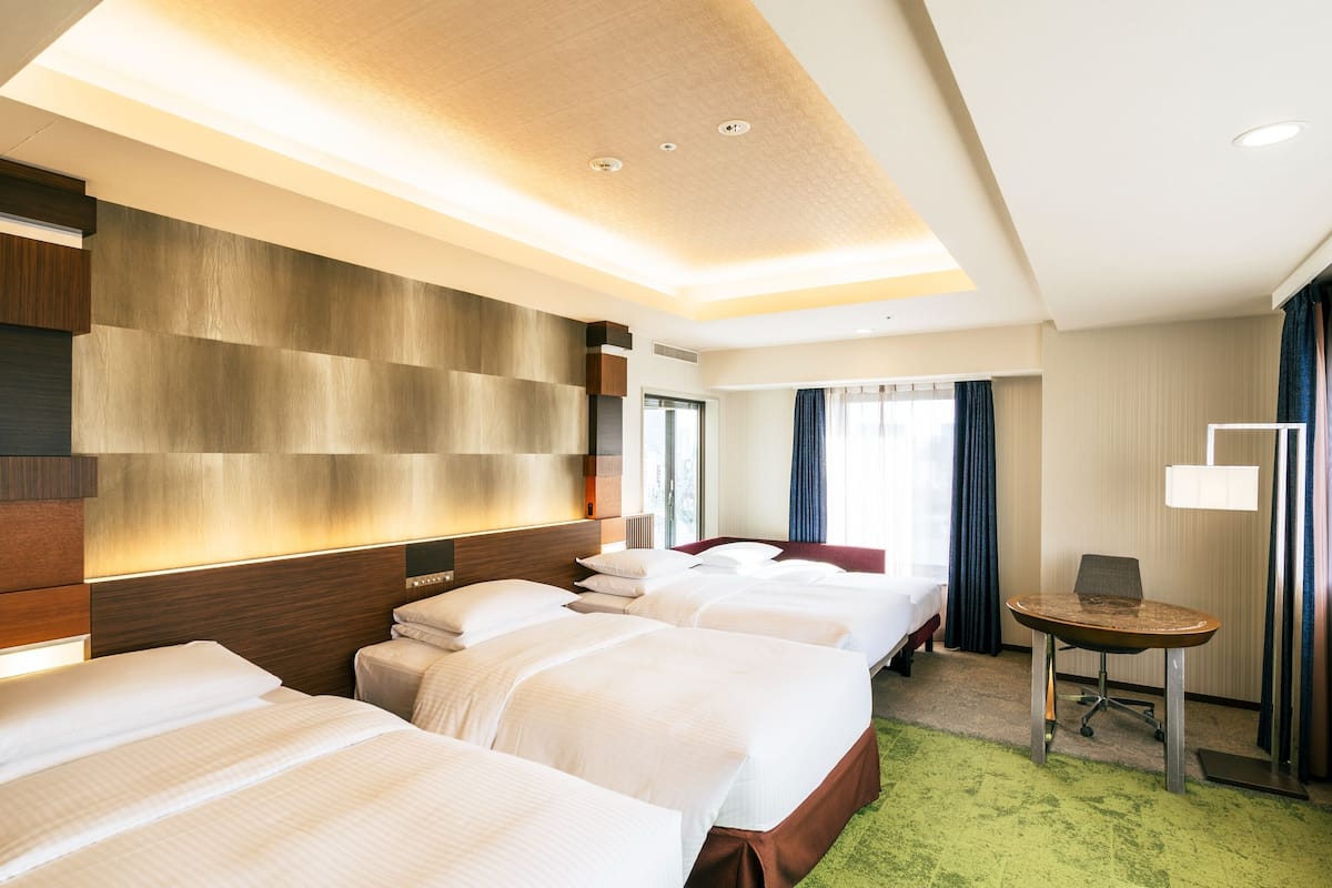 Habitación de hotel con tres camas, un escritorio y una silla.