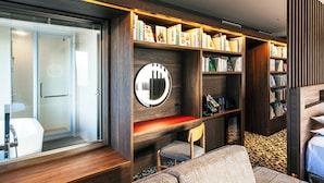 Une chambre d’hôtel moderne avec une bibliothèque en bois, un miroir rond, un coin salon et une douche.