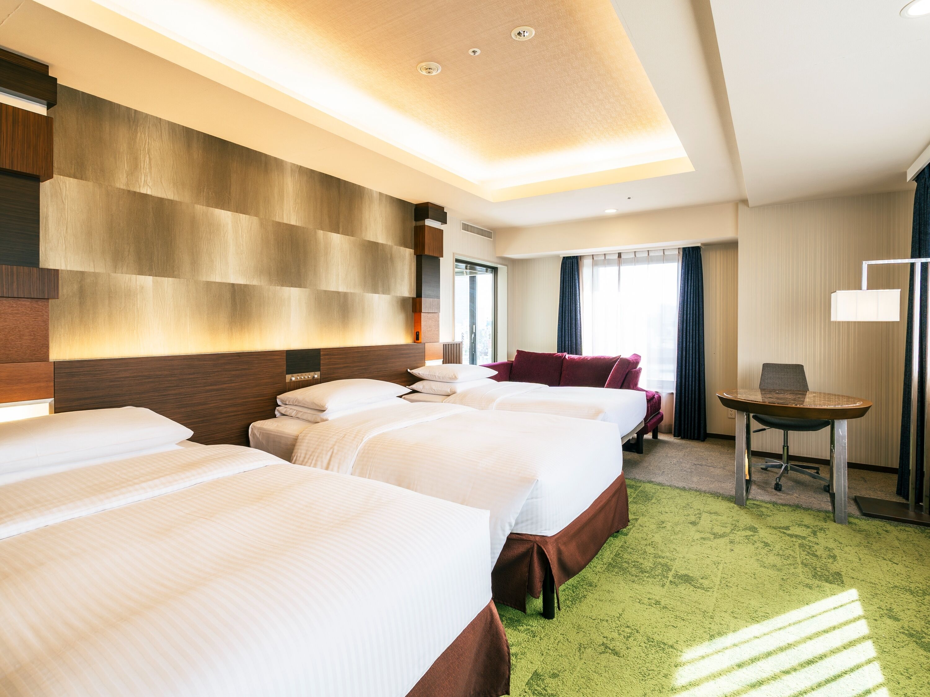 Une chambre d’hôtel avec trois lits, un bureau et une moquette verte.