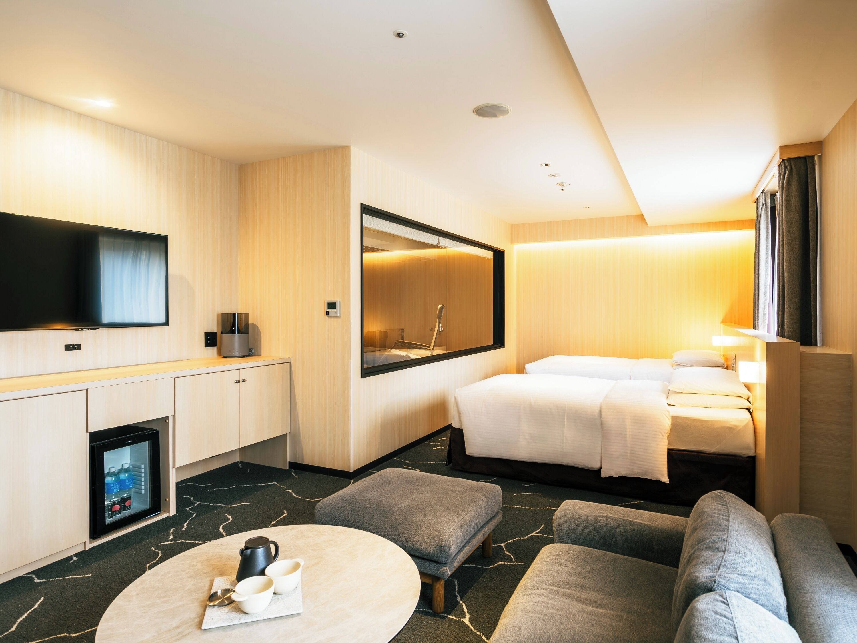 A hotel room with a bed, a TV, a mini-fridge, a coffee table, and a seating area.