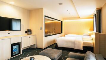 A hotel room with a bed, a TV, a mini-fridge, a coffee table, and a seating area.