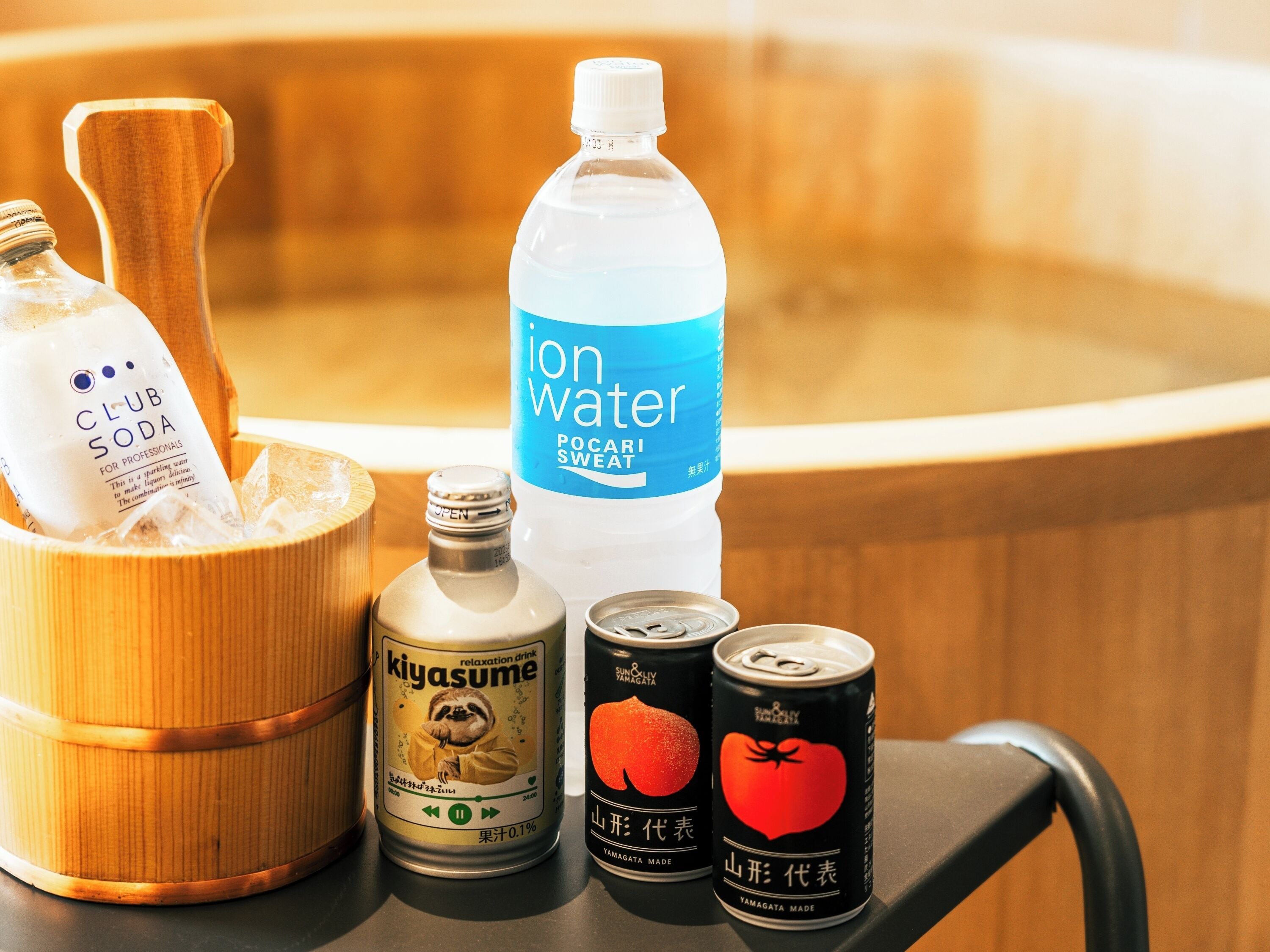 A wooden tub filled with ice, a bottle of ion water, a can of kiyasume, and a can of Yamagata made drink.