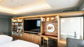 A hotel room with a large TV, wooden bookshelves, a desk, and a large mirror.