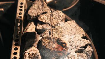 A grill with charcoal and a metal container, likely for fuel or seasoning.