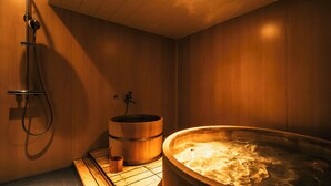 Un sauna avec une baignoire en bois, un banc en bois et une pomme de douche.