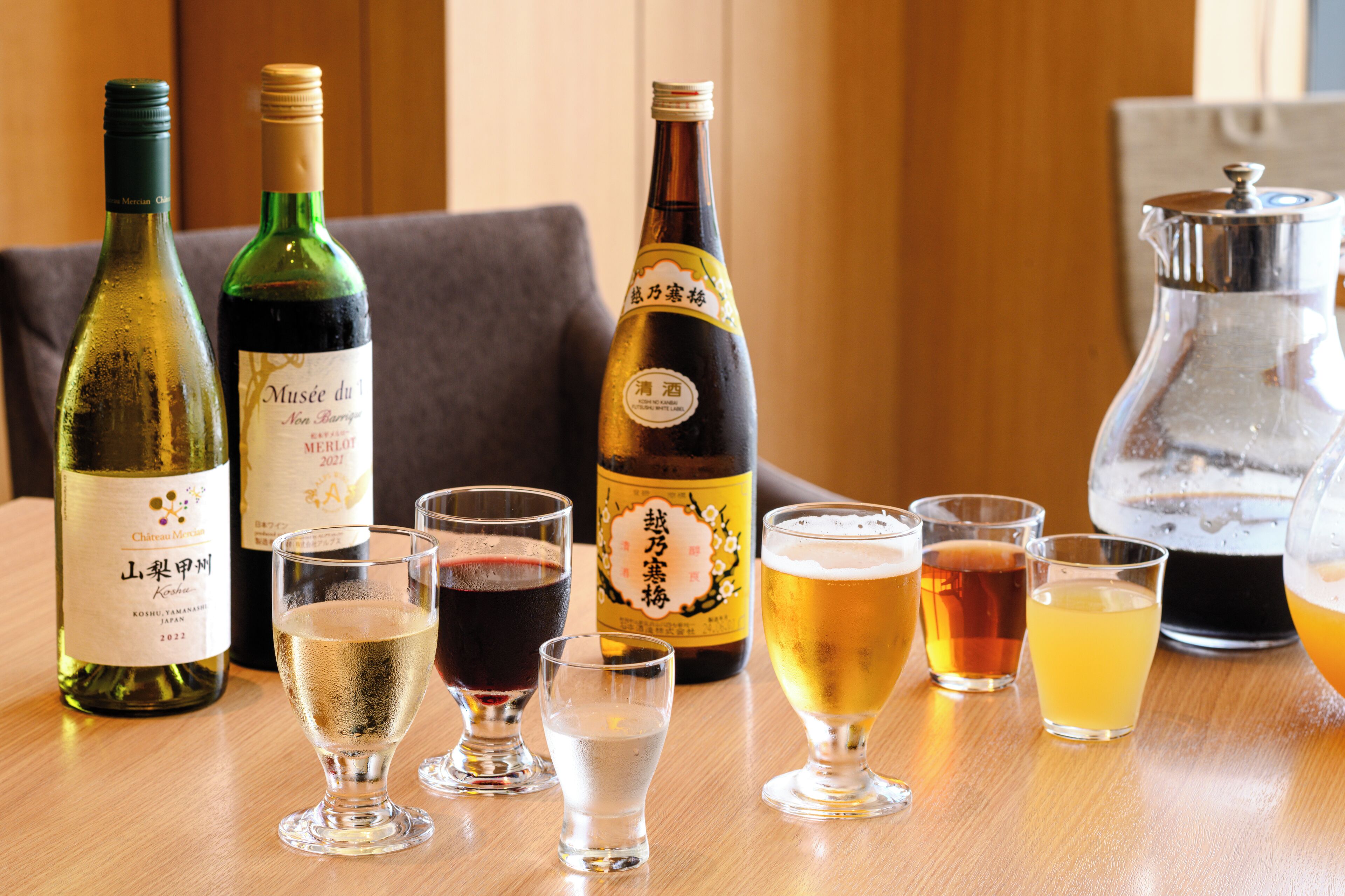 Ein Holztisch mit verschiedenen Flaschen und Gläsern mit Getränken, darunter Wein und Bier.