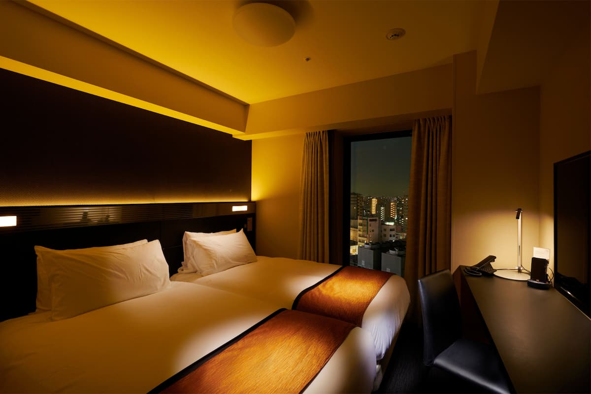 A hotel room with a large bed, a desk with a chair, and a view of the city at night.