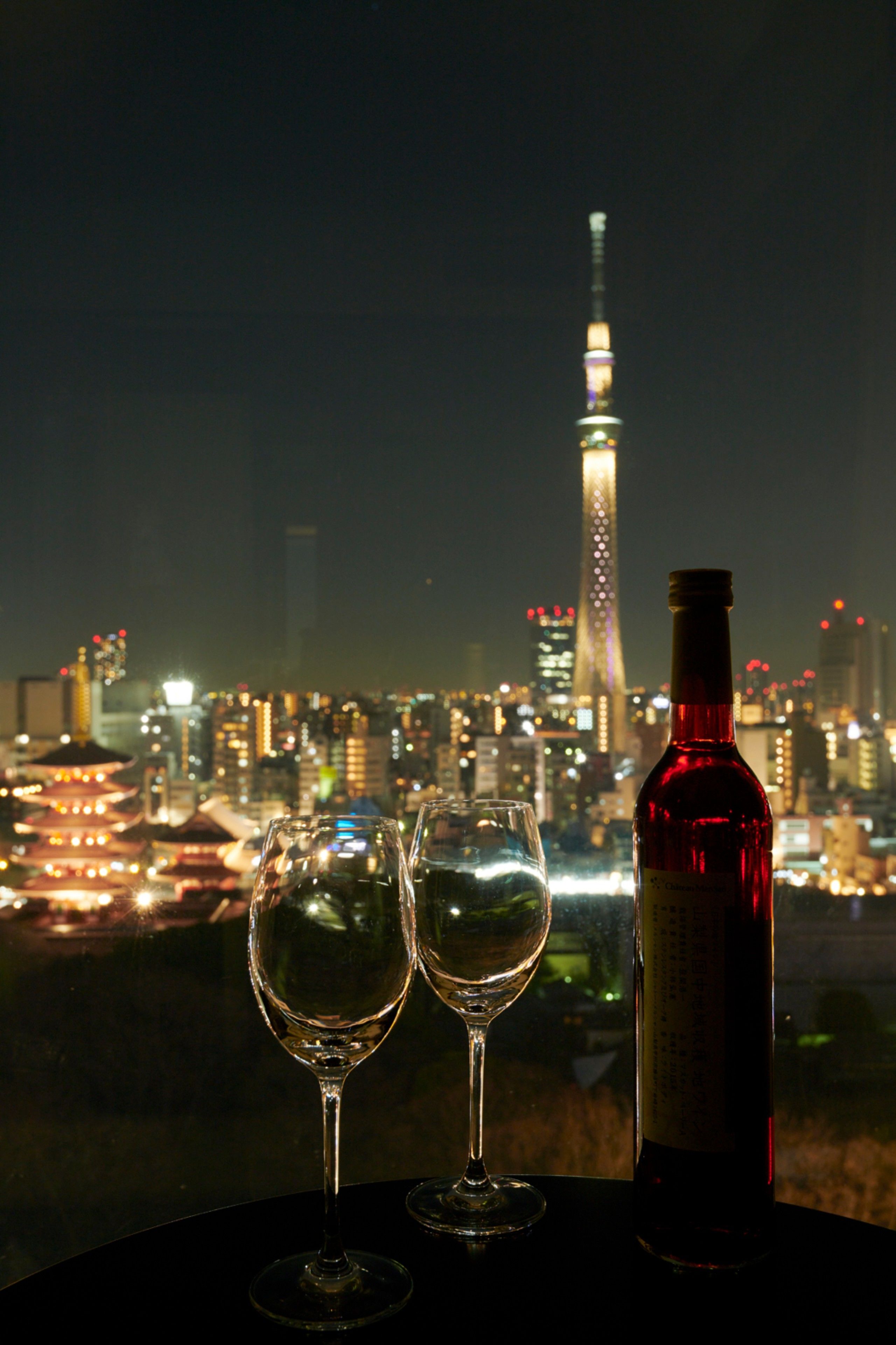 Two wine glasses and a bottle on a table with a cityscape and a tower in the background.
