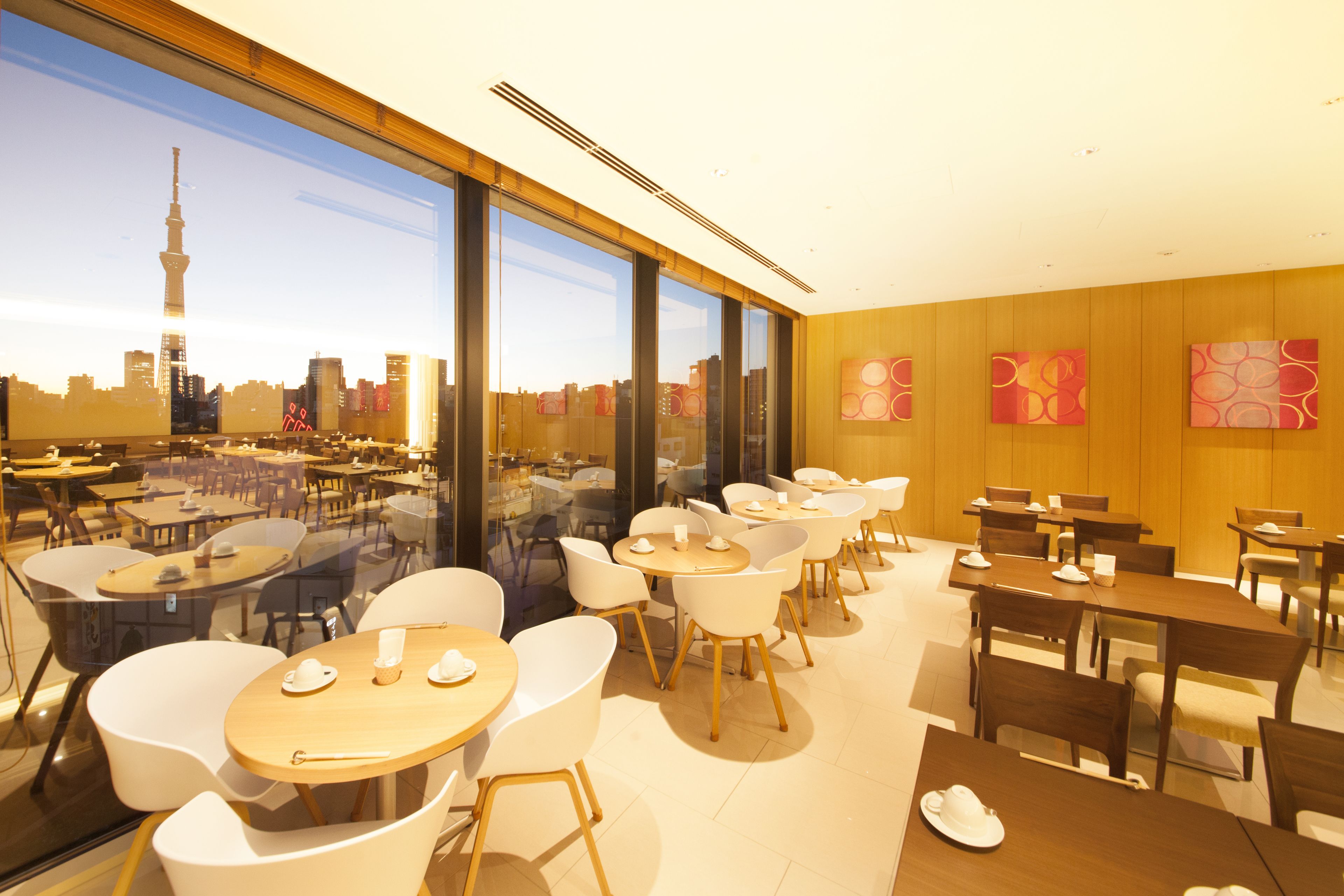 A modern dining area with tables and chairs, large windows with a city skyline view, and wooden paneling on the walls.