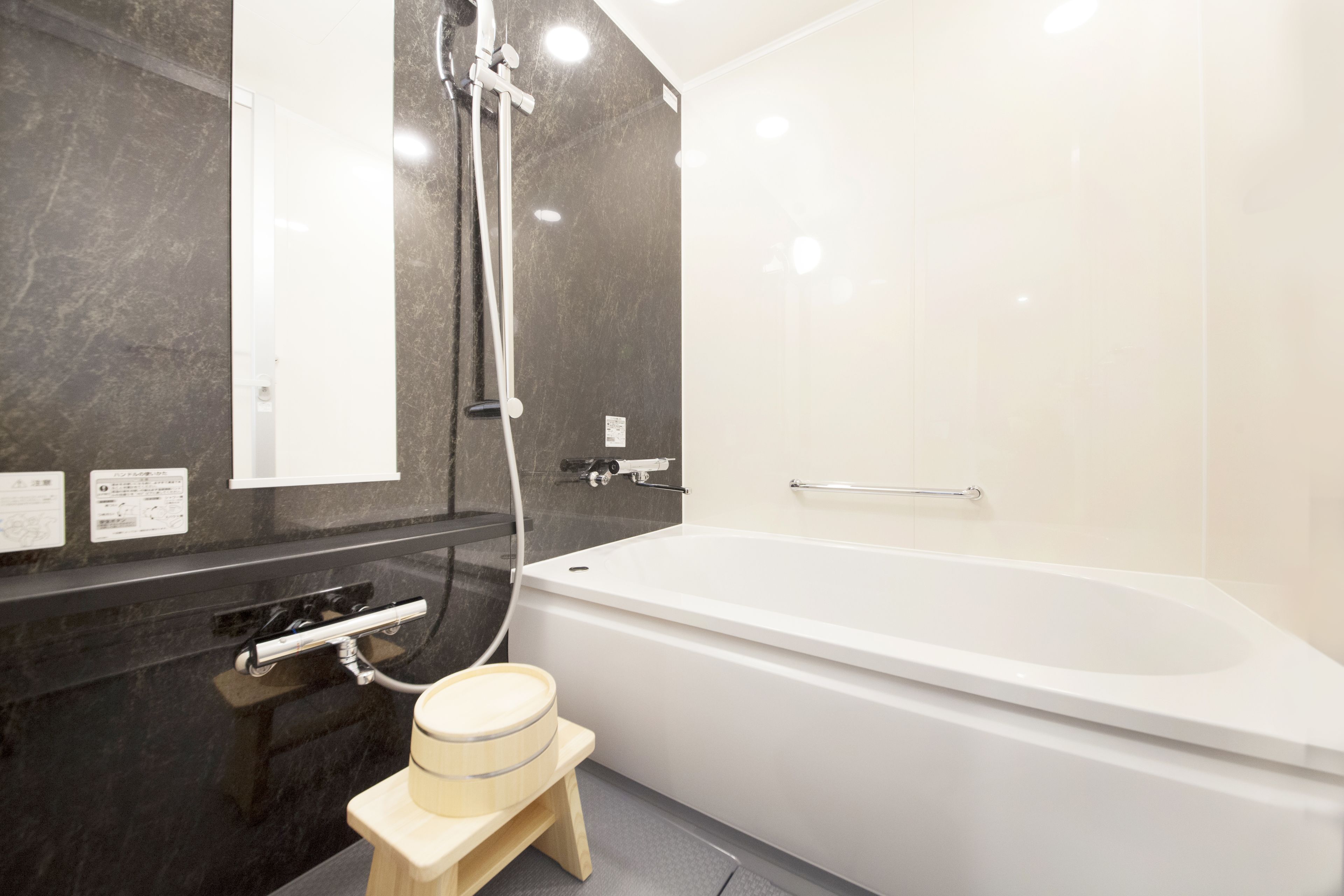 A modern bathroom with a white bathtub, a wooden stool, a glass-enclosed shower, and a marble wall.