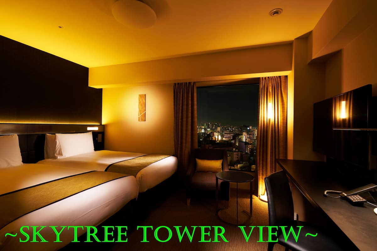 A hotel room with a bed, a desk, a chair, and a view of the city at night.