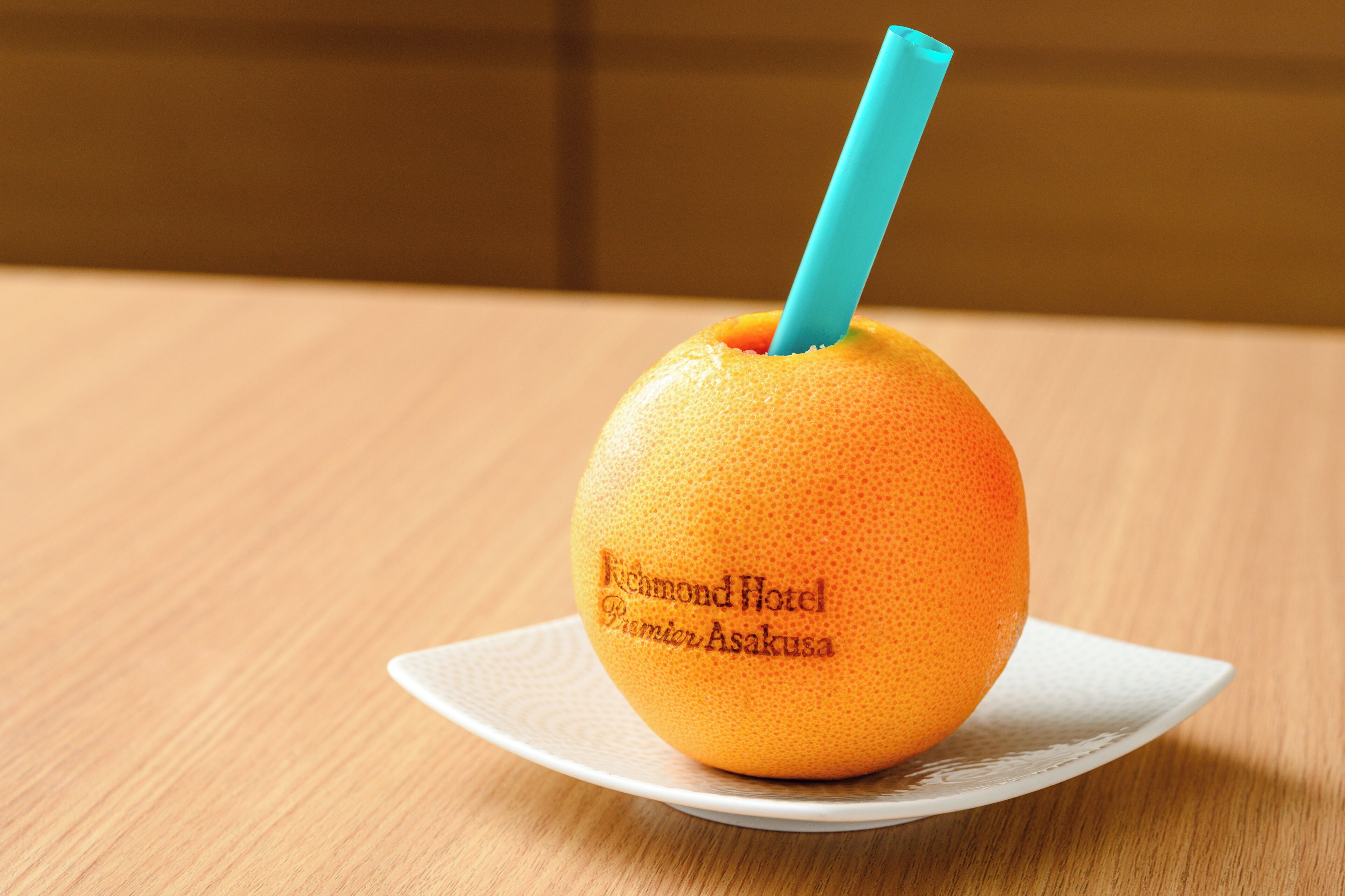 A single orange with a blue straw on a white plate, placed on a wooden table.
