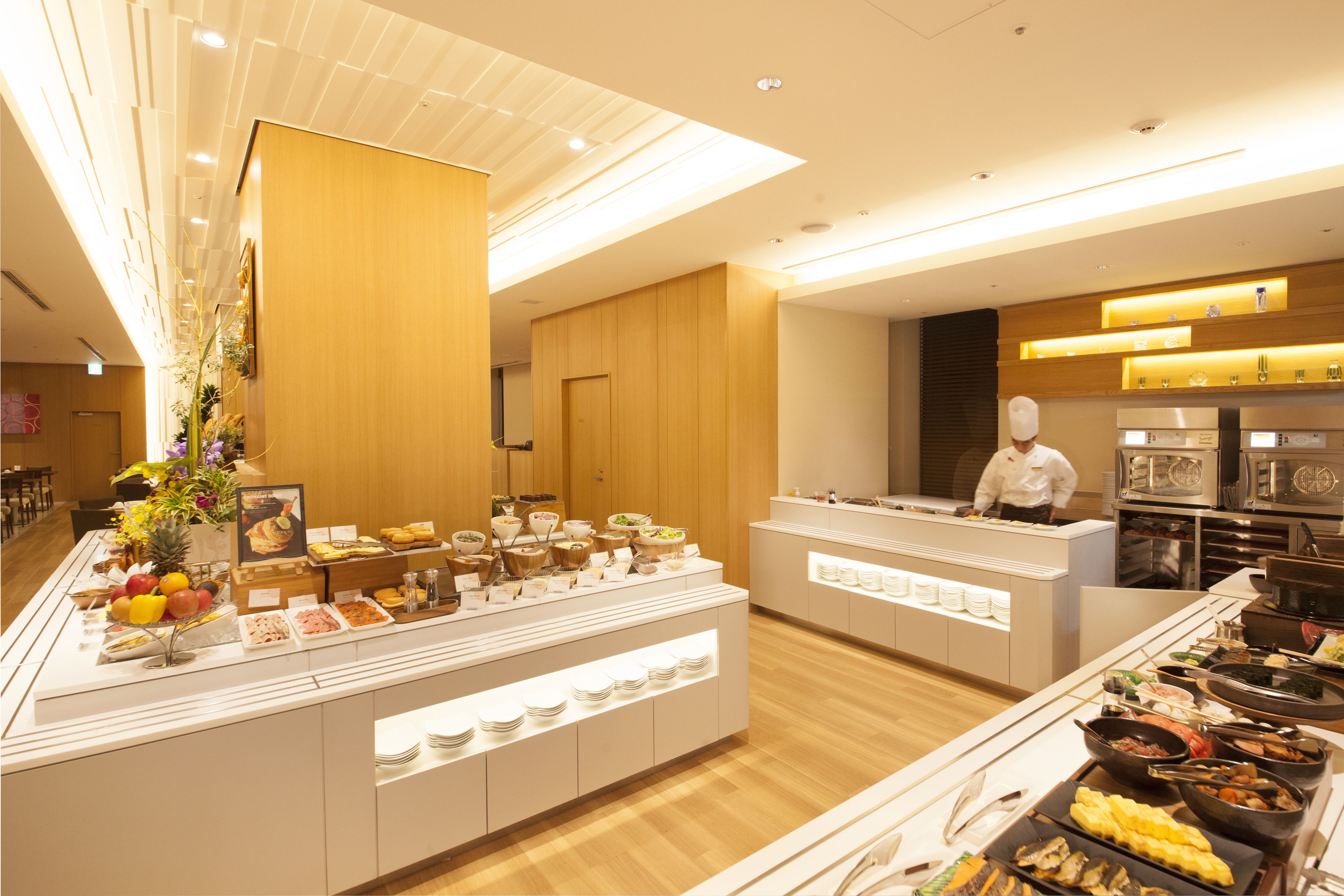 Een buffet met diverse gerechten, een kok die eten bereidt, en een modern interieur.