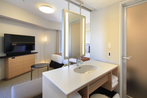 Un baño de hotel moderno con un espejo grande, un lavamanos, un televisor y una mesita.