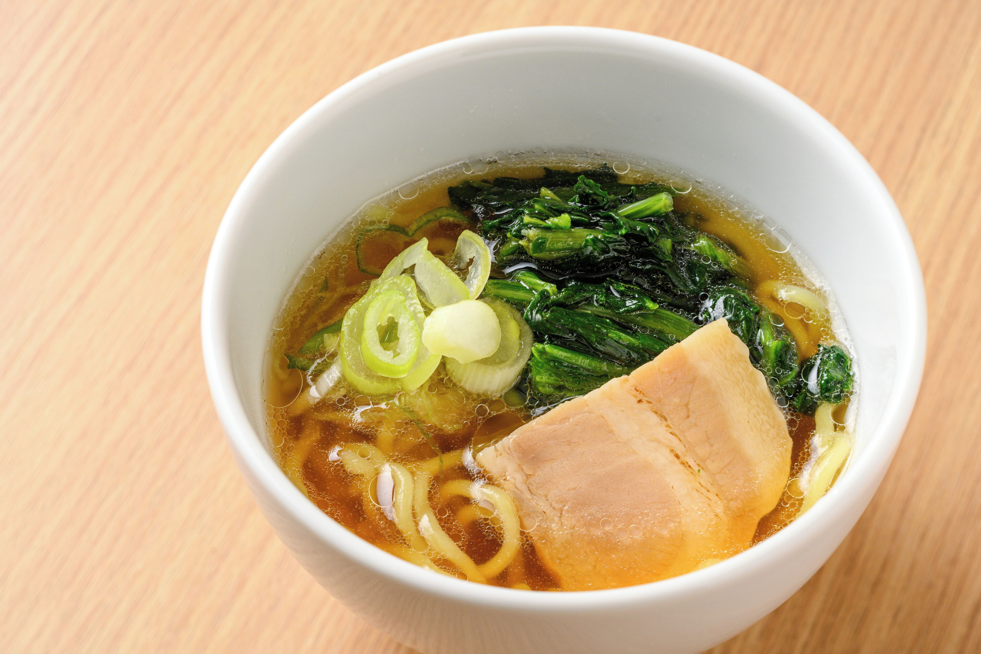 A bowl of soup with noodles and vegetables on a wooden table.