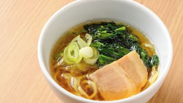 A bowl of soup with noodles and vegetables on a wooden table.