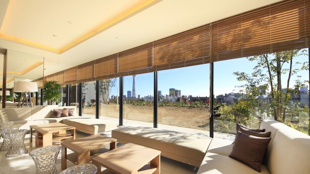 A modern living room with a sofa, coffee table, and chairs, large windows with blinds, and a city view. - Richmond Hotel Premier Asakusa International (Tokyo)