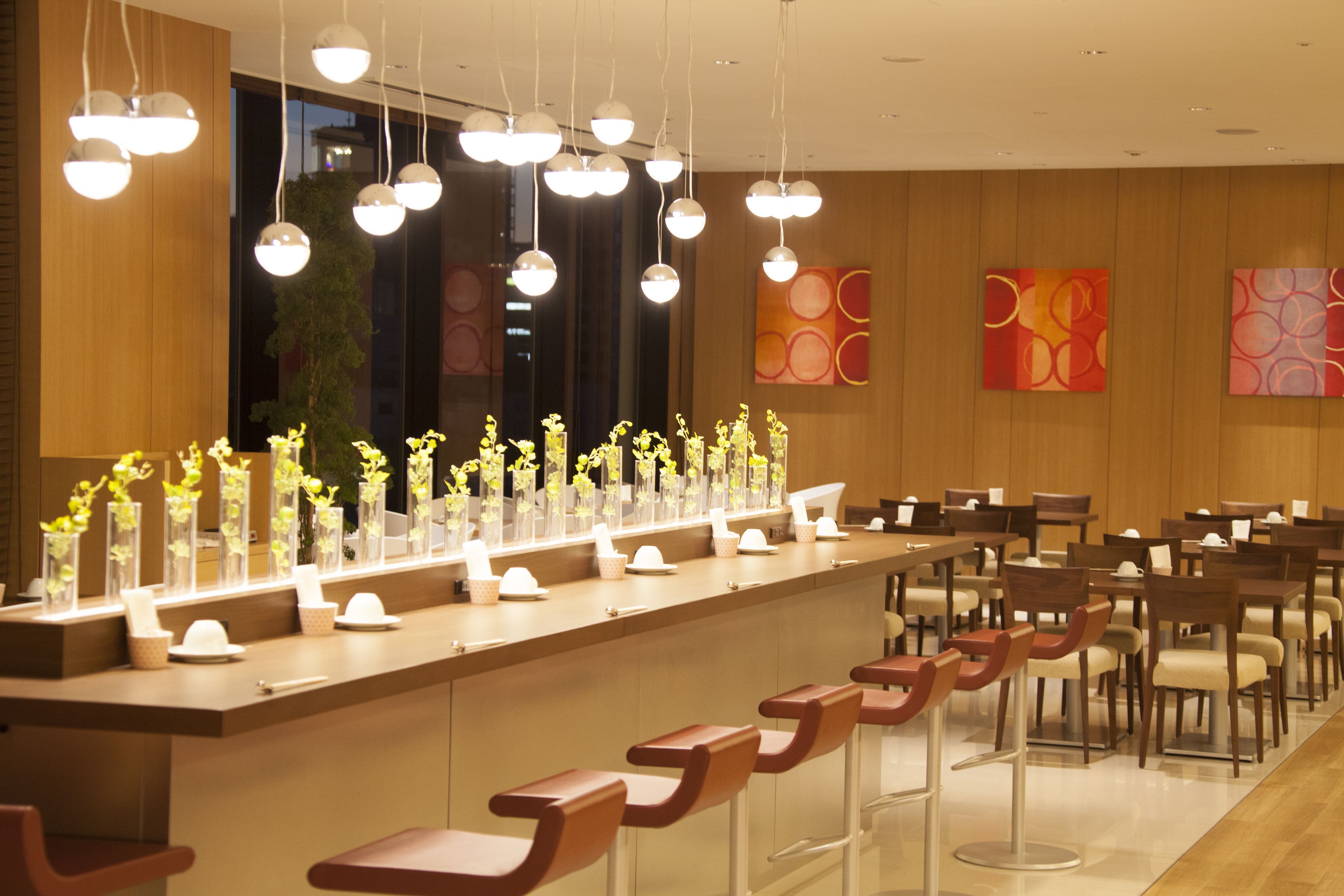 Eine moderne Bar mit einer langen Theke, mehreren hängenden Lampen und einer Reihe von Barhocker.