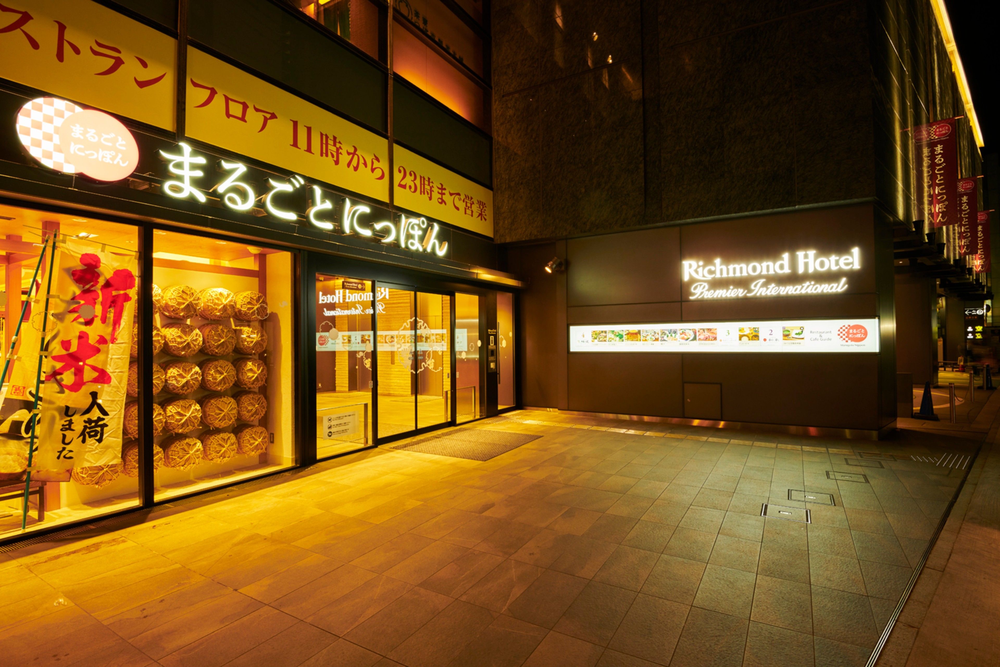 A hotel exterior at night with illuminated signage and a tiled pavement.