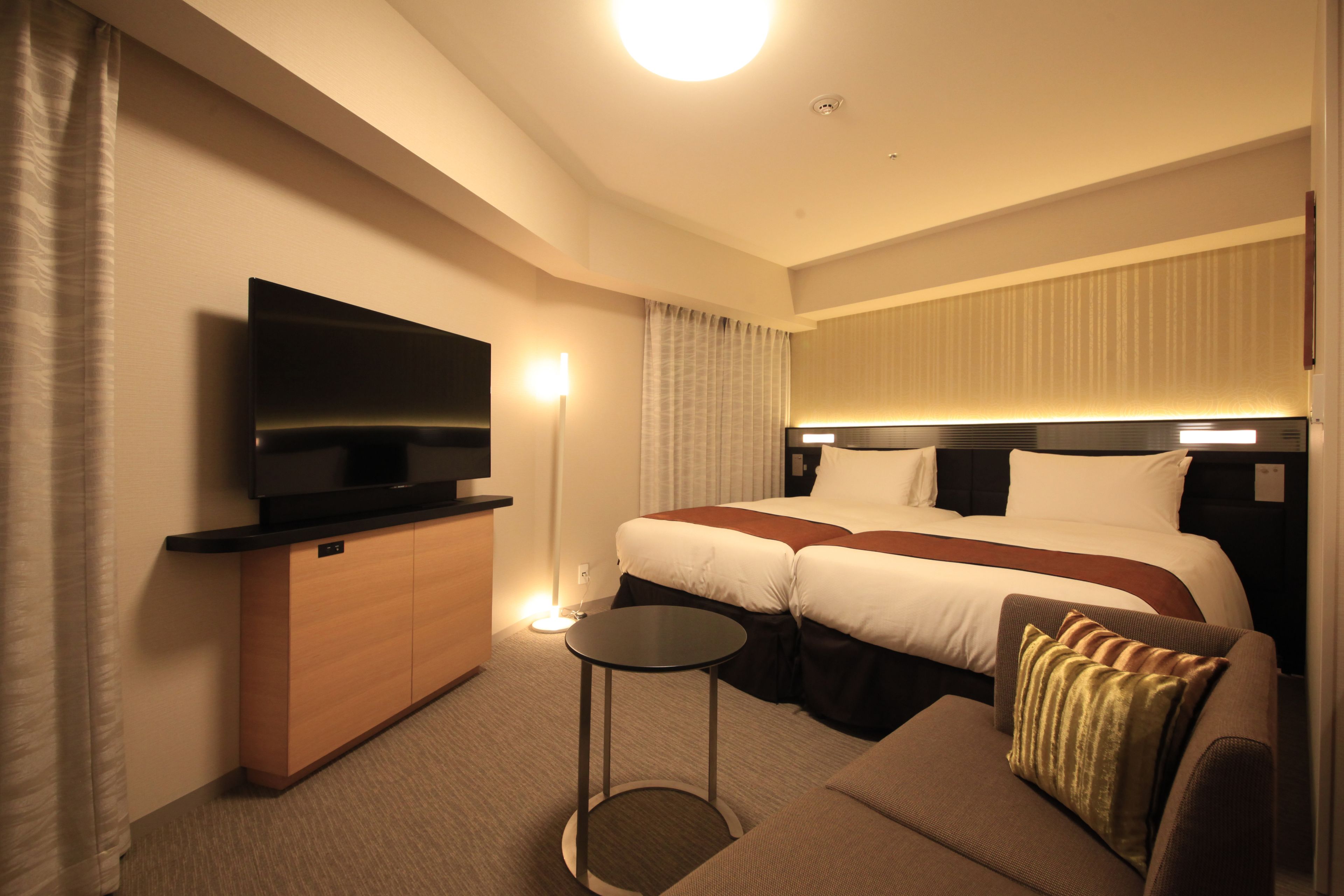 A hotel room with a bed, a TV, a small table, and a sofa.