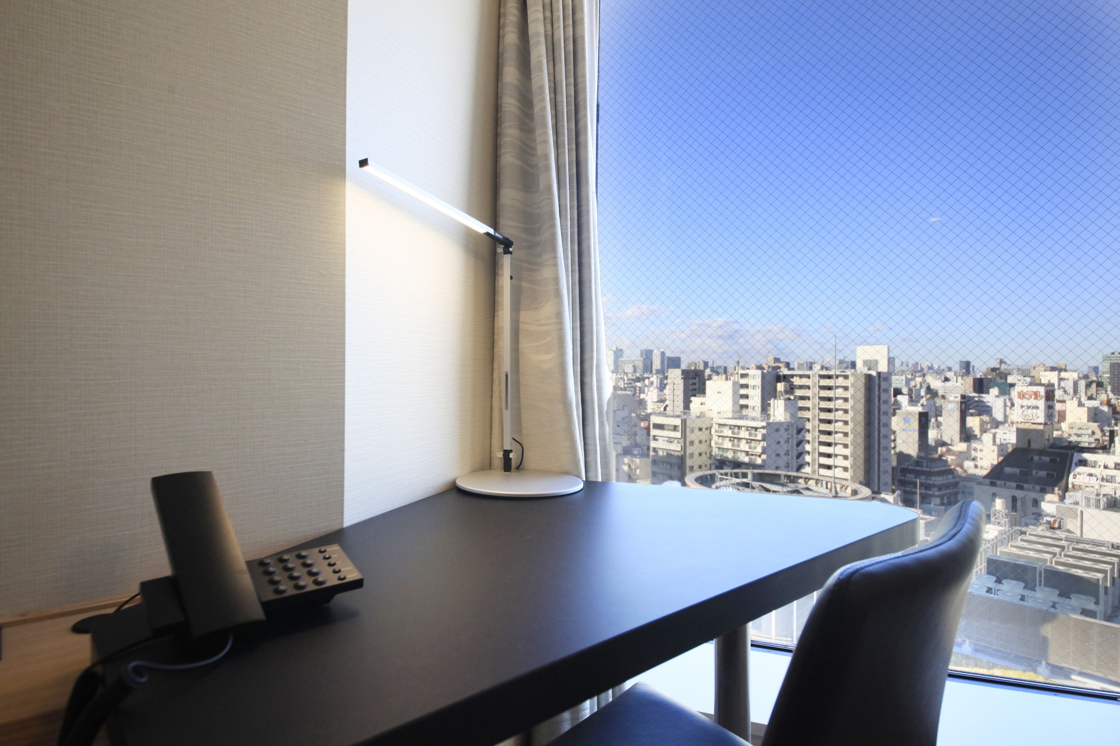 Une chambre d’hôtel équipée d’un bureau, d’une lampe, d’un téléphone et offrant une vue sur le paysage urbain par une fenêtre.