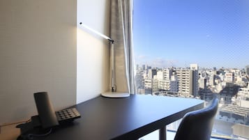 Une chambre d’hôtel équipée d’un bureau, d’une lampe, d’un téléphone et offrant une vue sur le paysage urbain par une fenêtre.