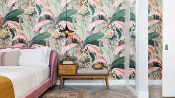 Un dormitorio con una cama grande, una mesita de noche, una lámpara y un papel tapiz tropical.