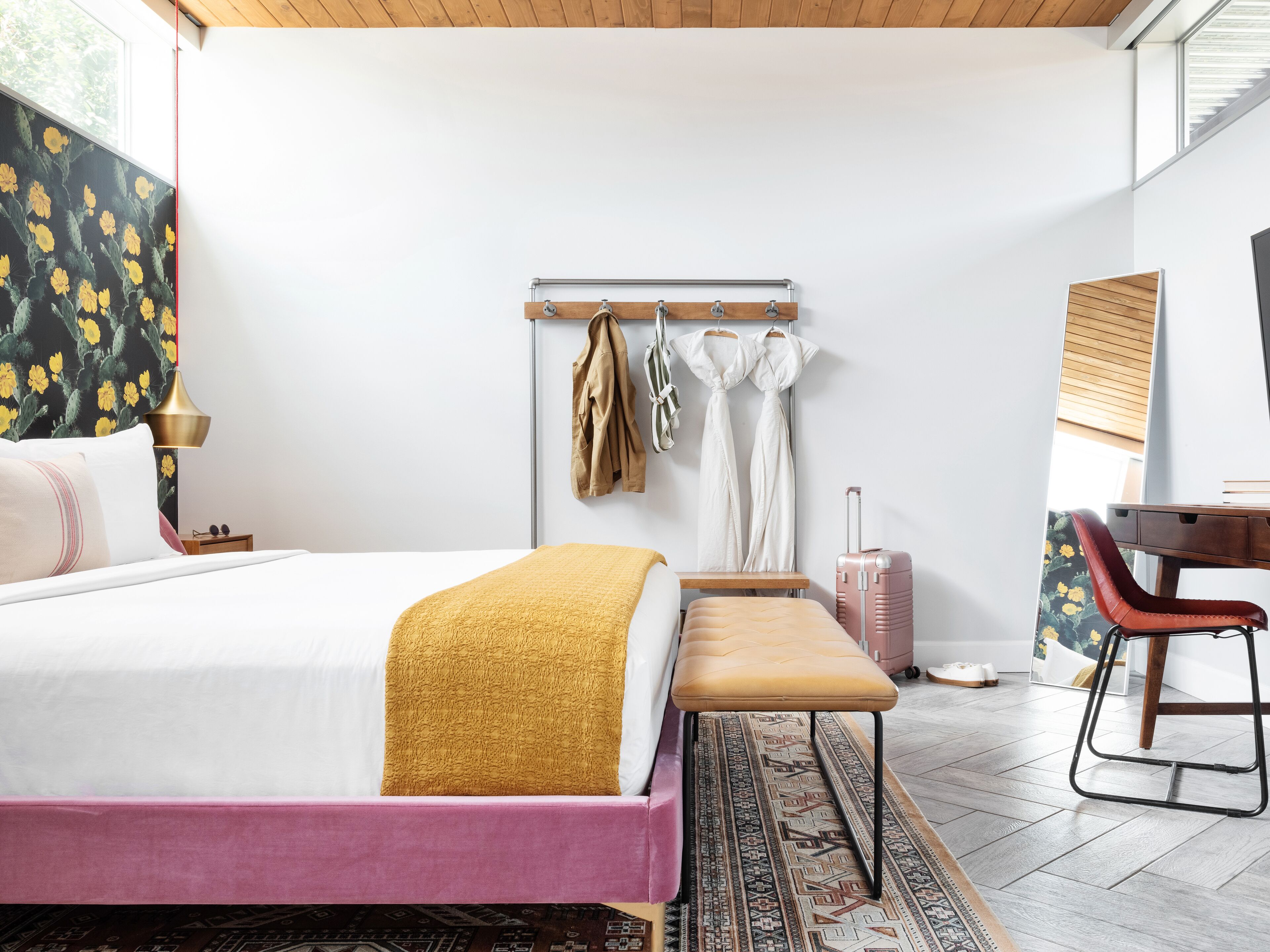 A modern bedroom with a bed, bench, desk, and a suitcase.