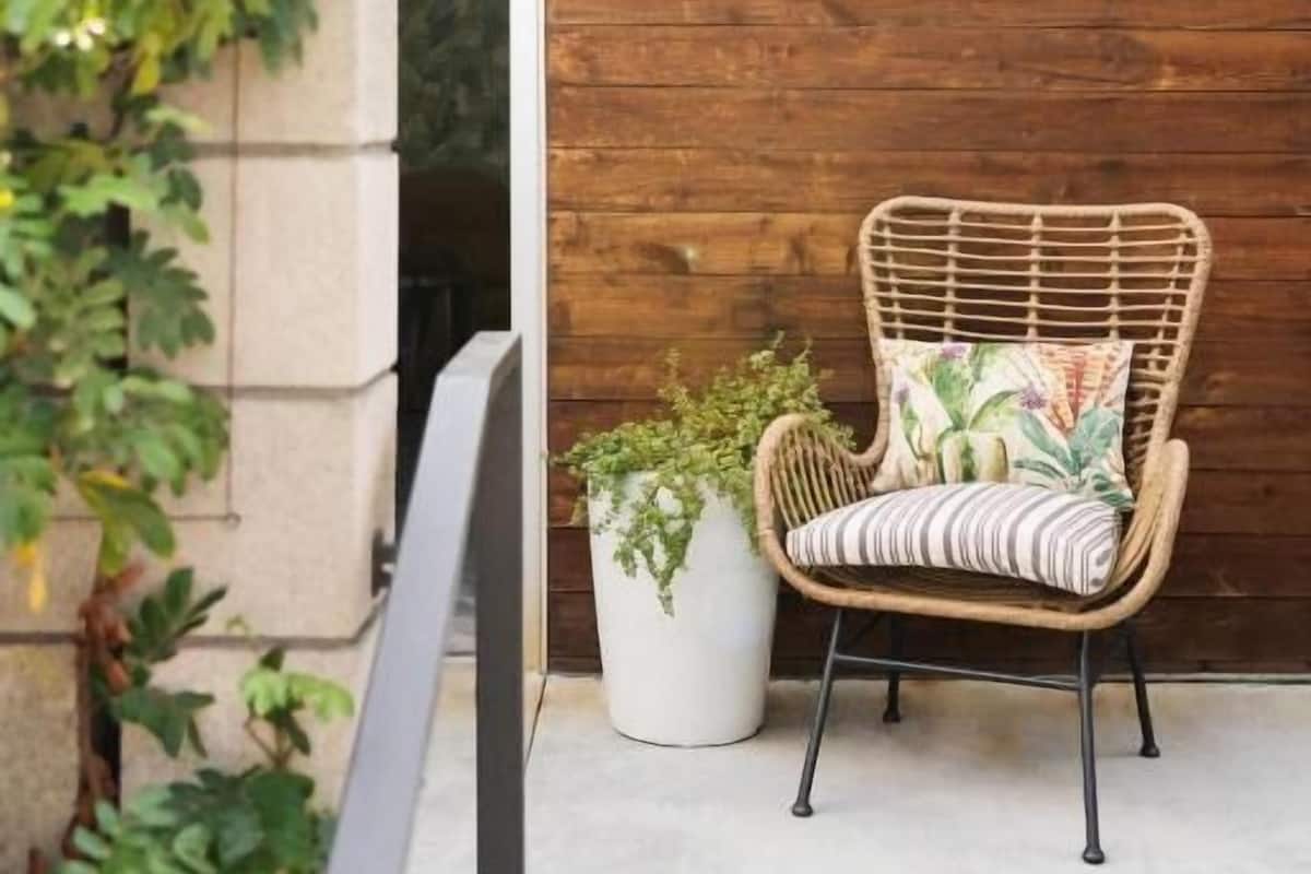 A wicker chair with a cushion, a potted plant, and a wooden wall with a number sign.