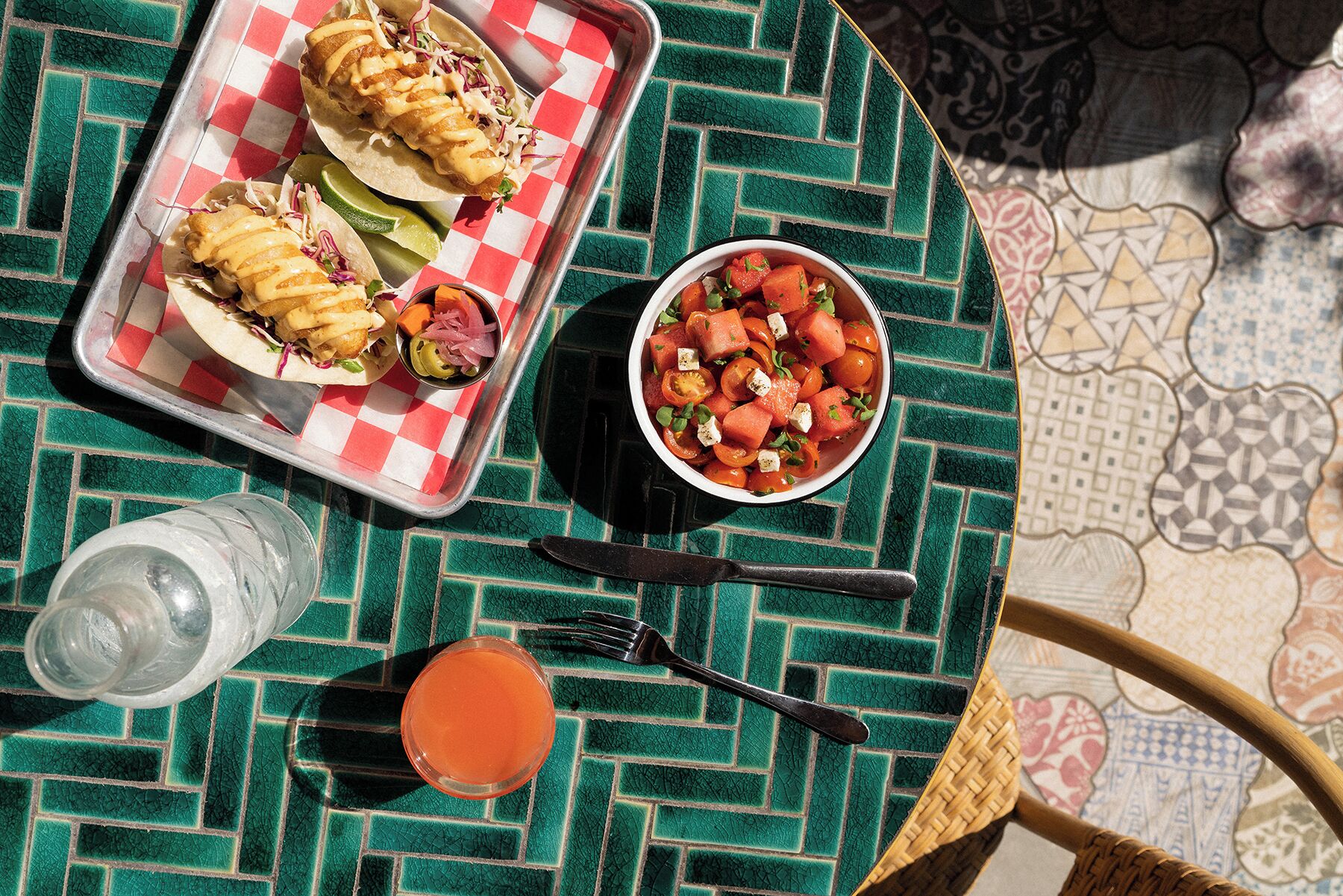 A meal setup with tacos, a bowl of salad, and a drink on a green patterned tablecloth.