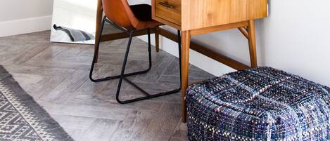 A modern workspace with a wooden desk, a black monitor, and a unique woven ottoman.