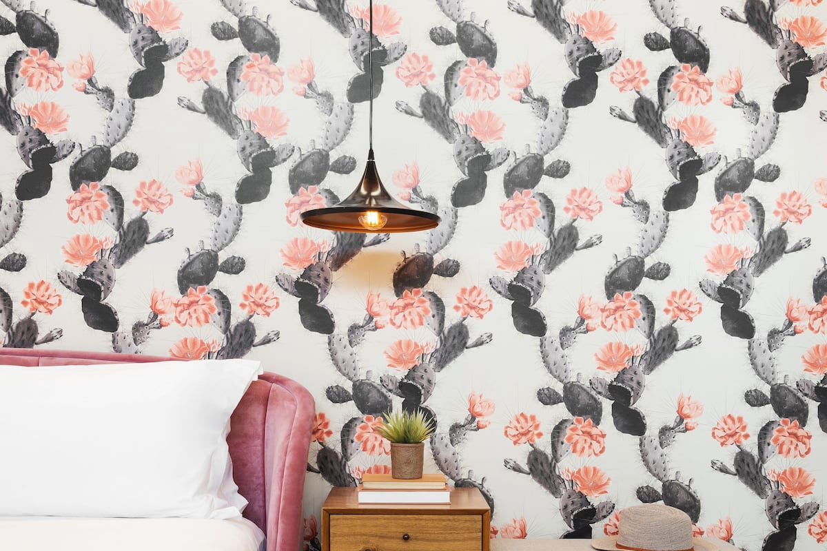 A bedroom with a bed, bedside table, lamp, and a patterned wall.