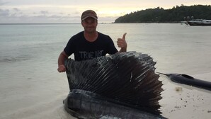 A man holding a large fish on a boat with a forested island in the background. - Family Song Bungalow (Koh Lipe)