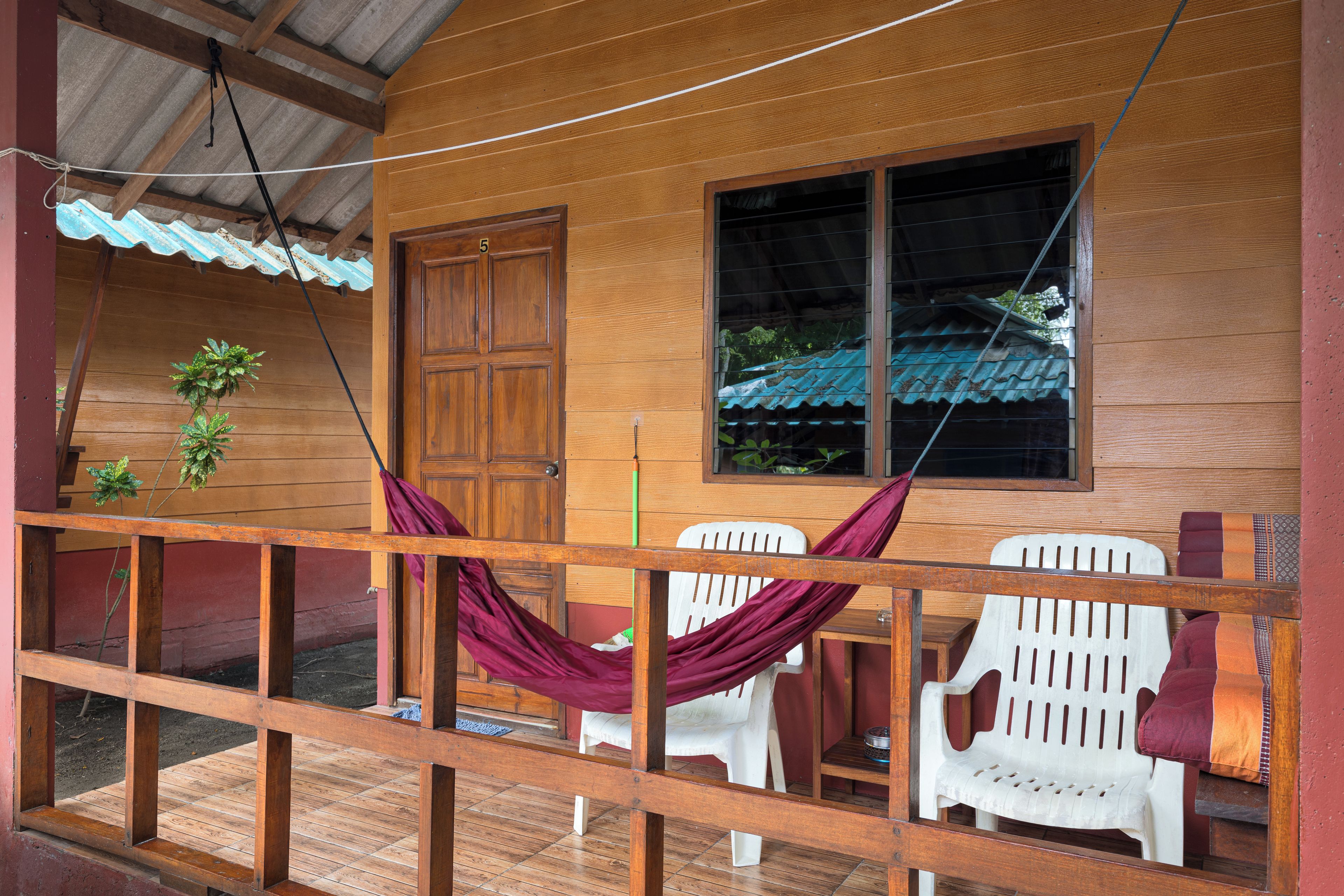 A wooden cabin with a porch, a hammock, and white plastic chairs.