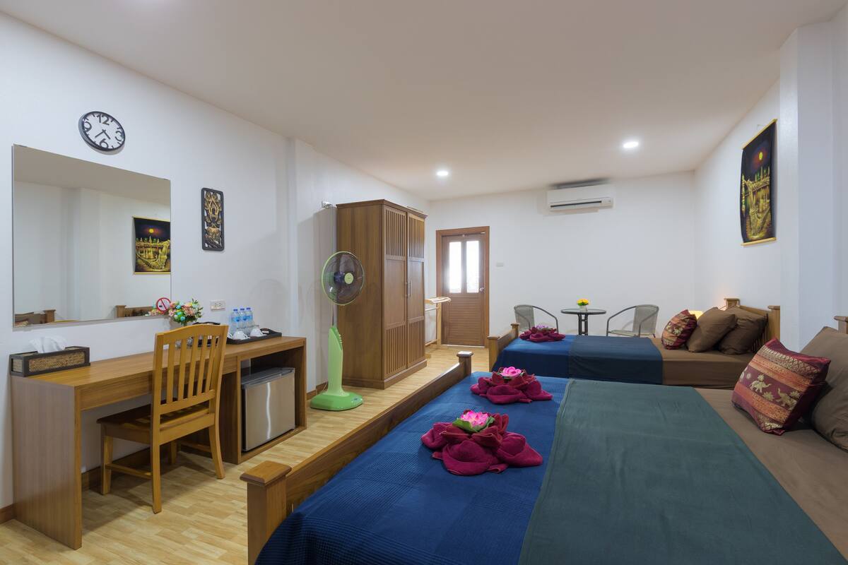 A hotel room with a wooden desk, a chair, a bed with blue bedding, a small table with a chair, and a wardrobe.
