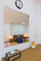 Un dormitorio con una cama, mesitas de noche, un espejo, un reloj, un florero y una caja de pañuelos.