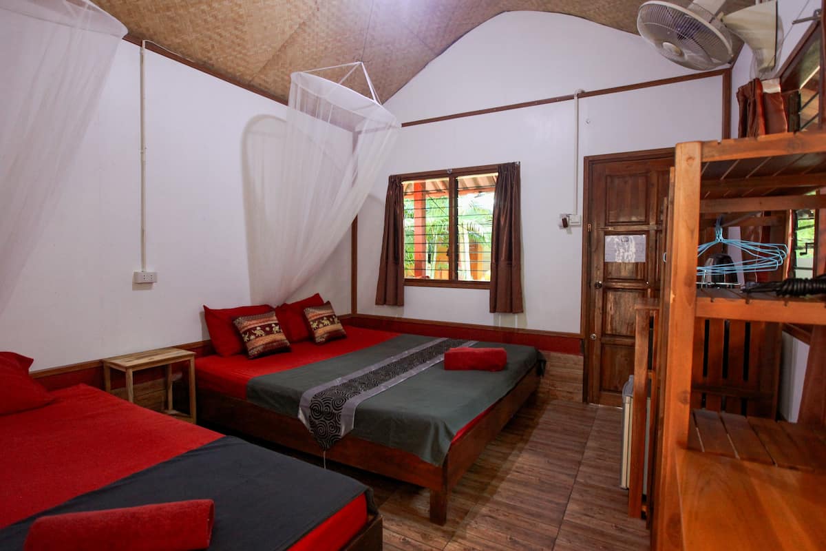 A room with two beds, a wooden ceiling, a window with curtains, and a fan.