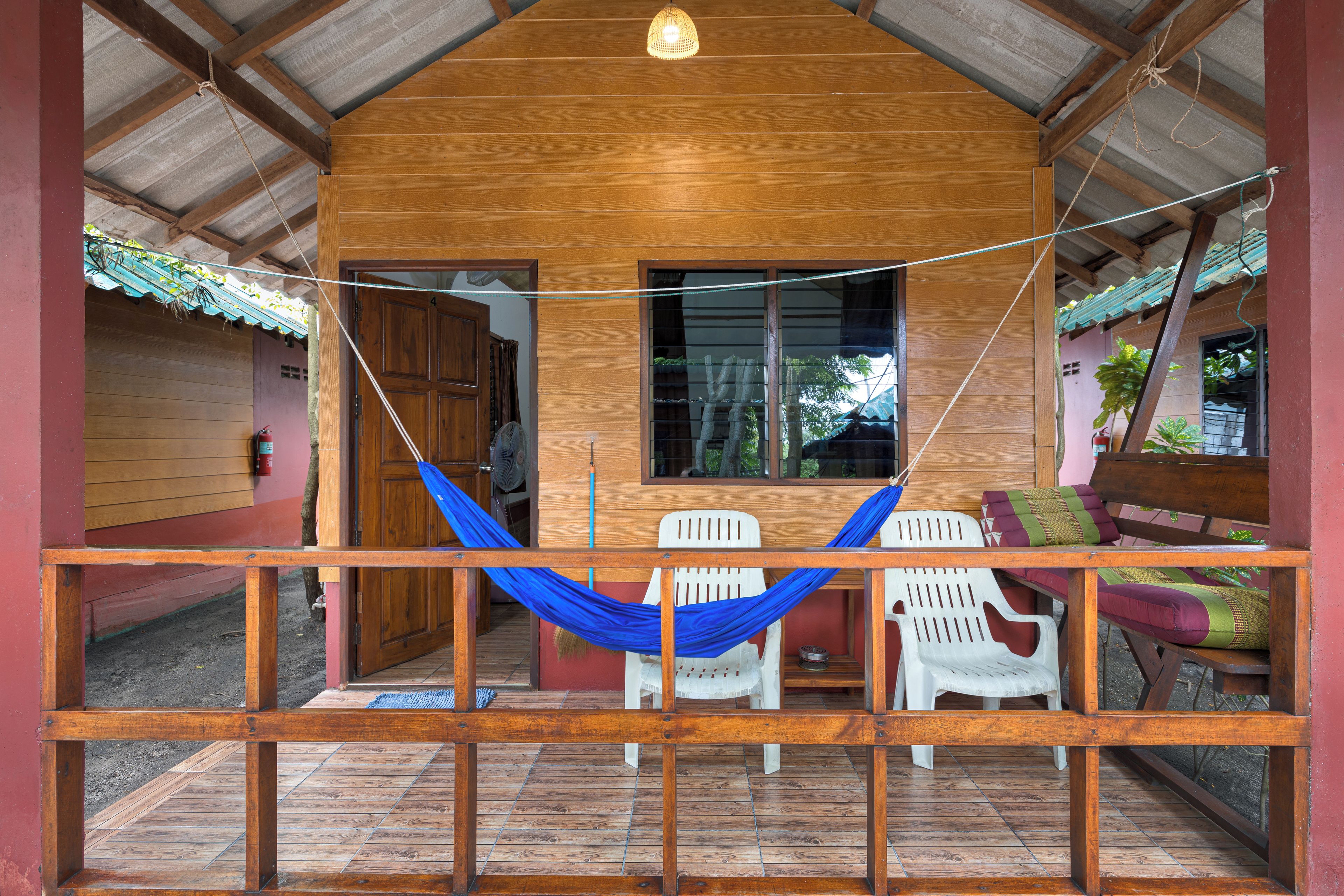 A wooden porch with a hammock, white plastic chairs, and a wooden table.