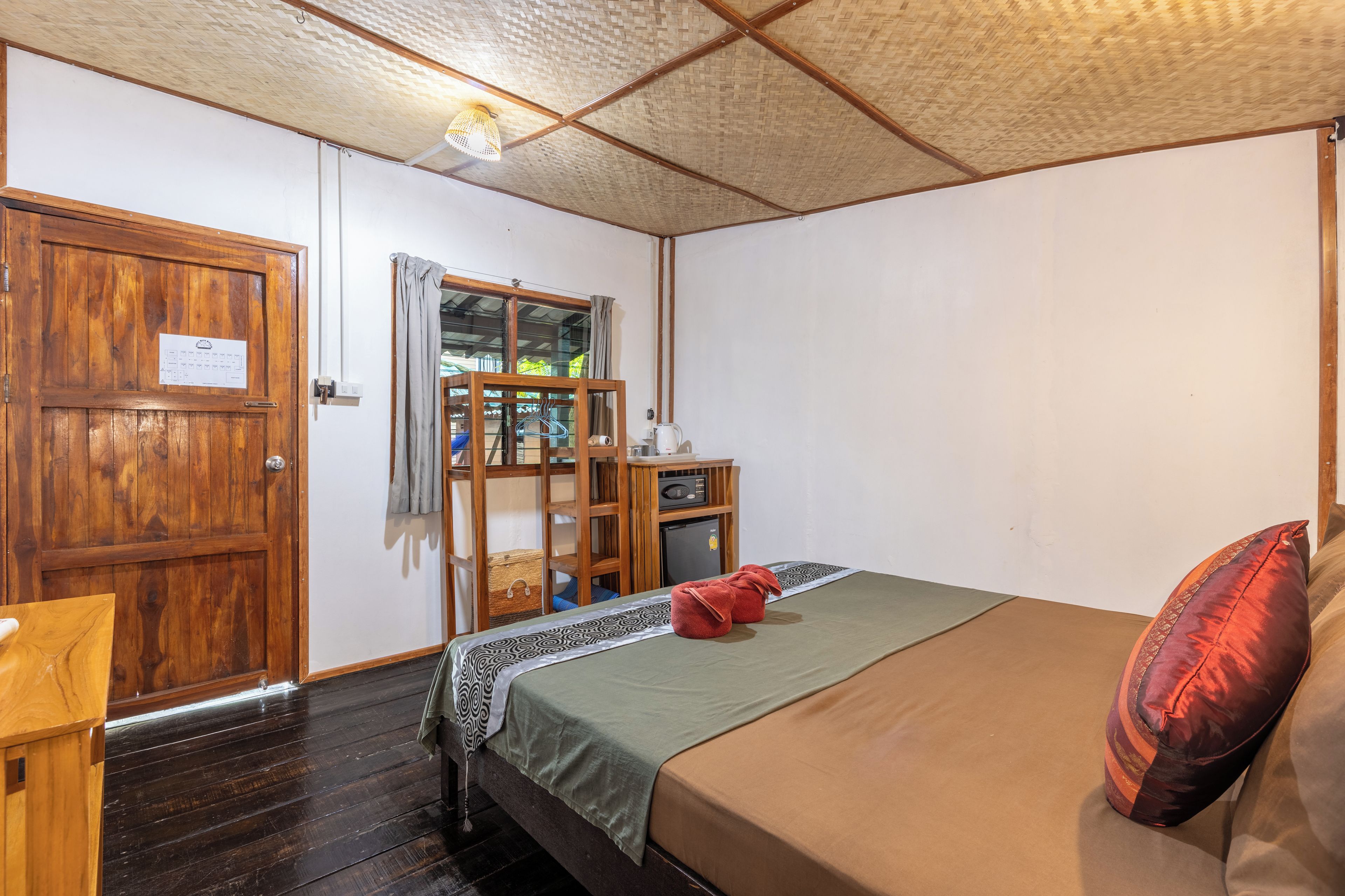 Quarto com cama, porta de madeira, mesinha e janela com cortinas.