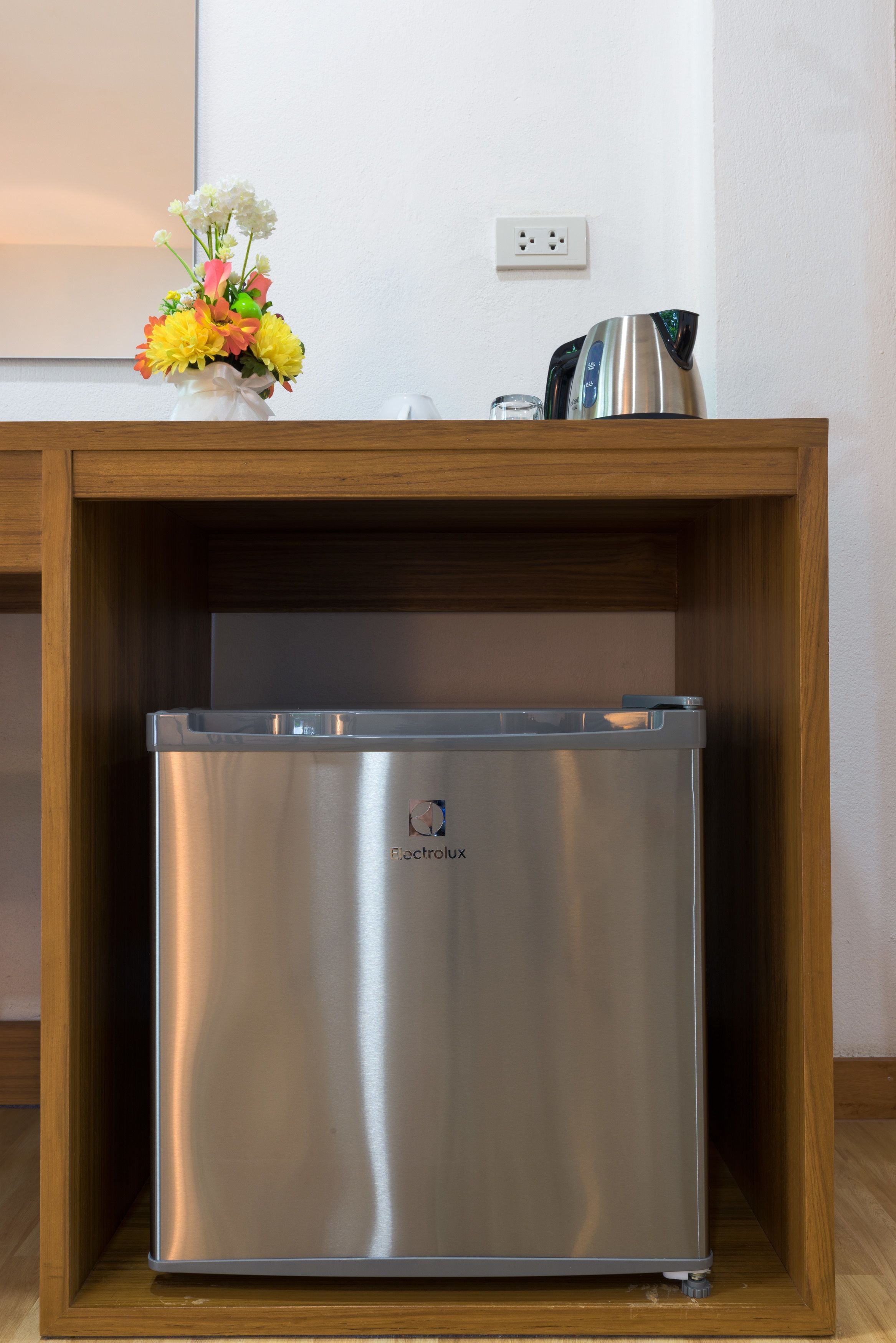 A compact, stainless steel refrigerator in a wooden cabinet with a vase of flowers on top.