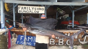A person holding a large fish in front of a building with a sign that reads "FAMILYSONG BUNGALOW". - Family Song Bungalow (Koh Lipe)