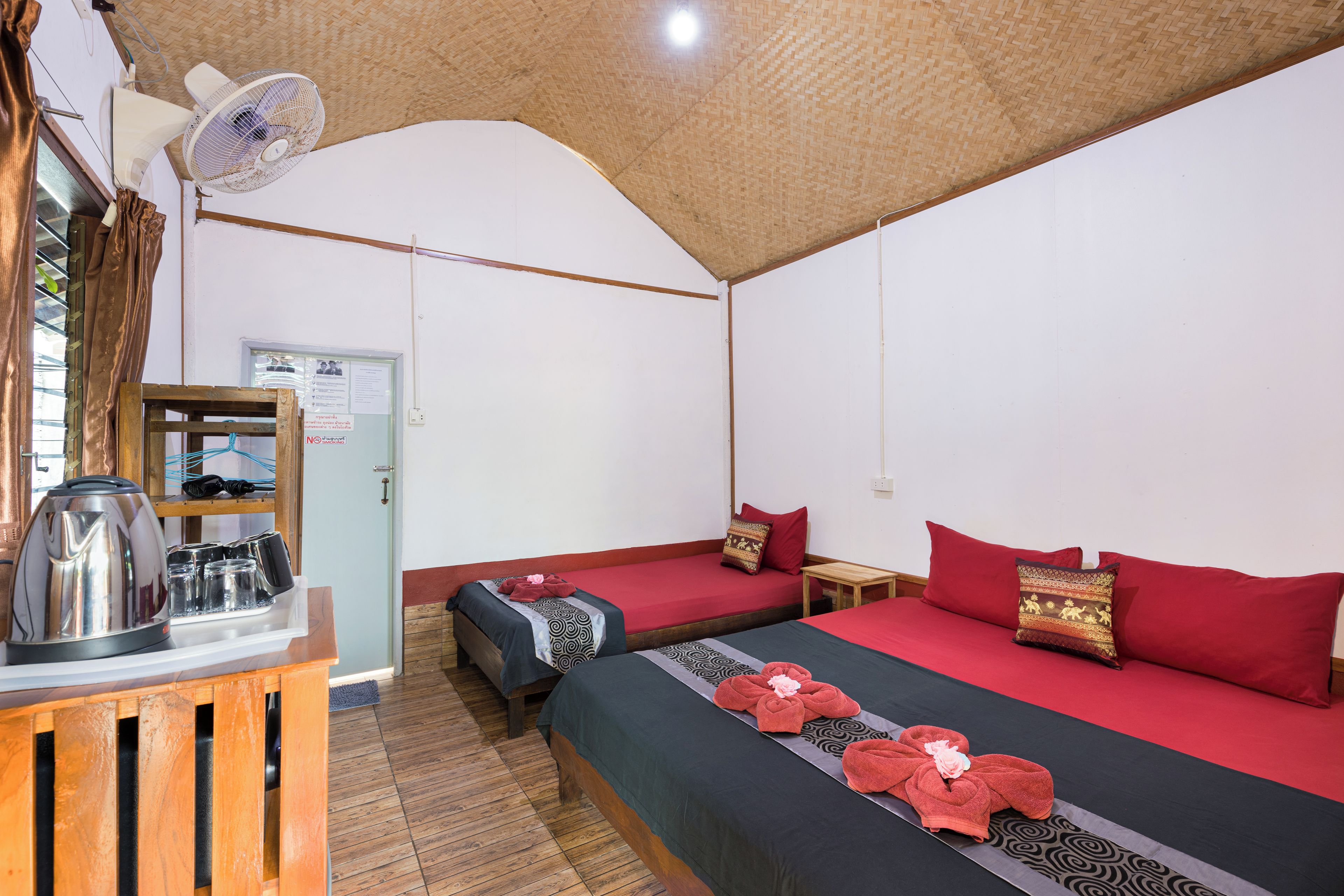 Ein Zimmer mit zwei Betten, einem Holztisch mit Wasserkocher und einem Deckenventilator.