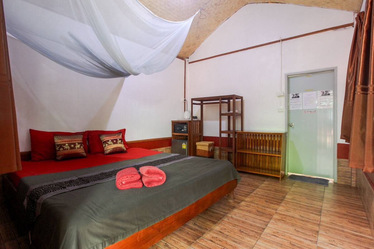 A bedroom with a bed, a wooden nightstand, a small table, and a door with a bulletin board.