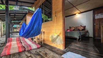 A wooden structure with a covered porch, a bed with pillows, and a blue hanging fabric.