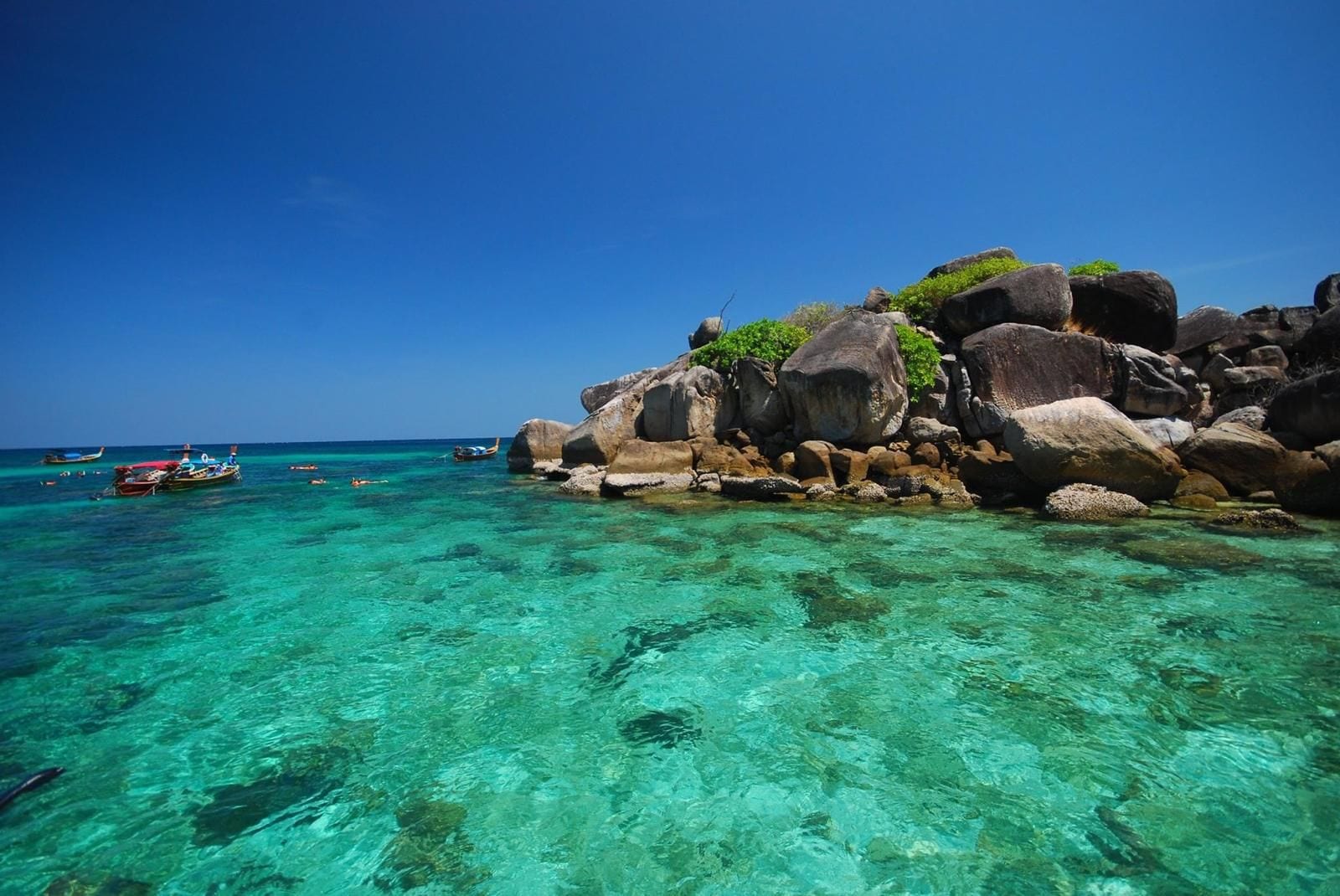 A clear turquoise sea with rocky formations and boats.