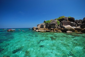 A clear turquoise sea with rocky formations and boats.