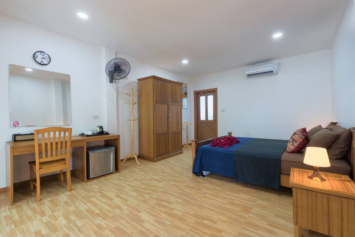 A bedroom with a bed, a desk, a chair, a wardrobe, and a bedside table with a lamp.