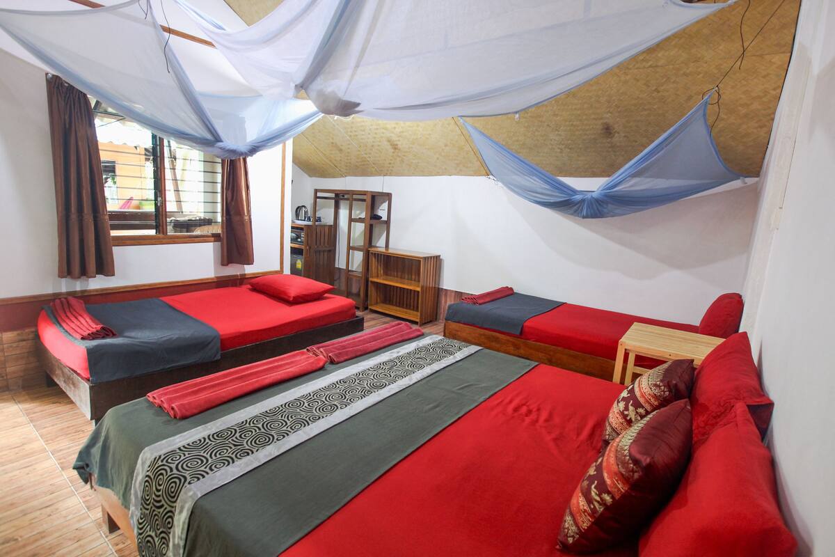 A room with two beds, a wooden desk, and a window with curtains.