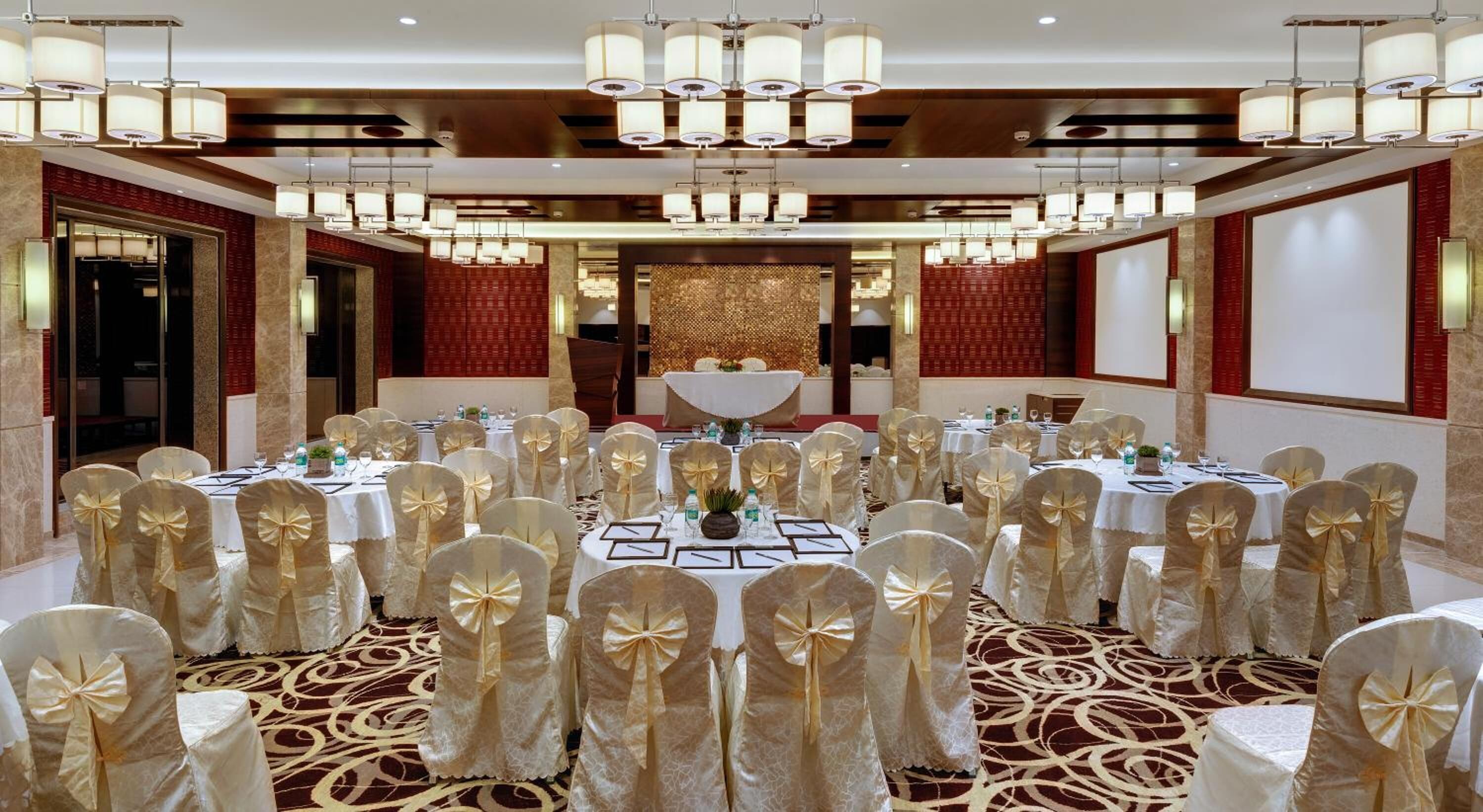 A banquet hall with round tables, chairs with gold bows, and a chandelier.